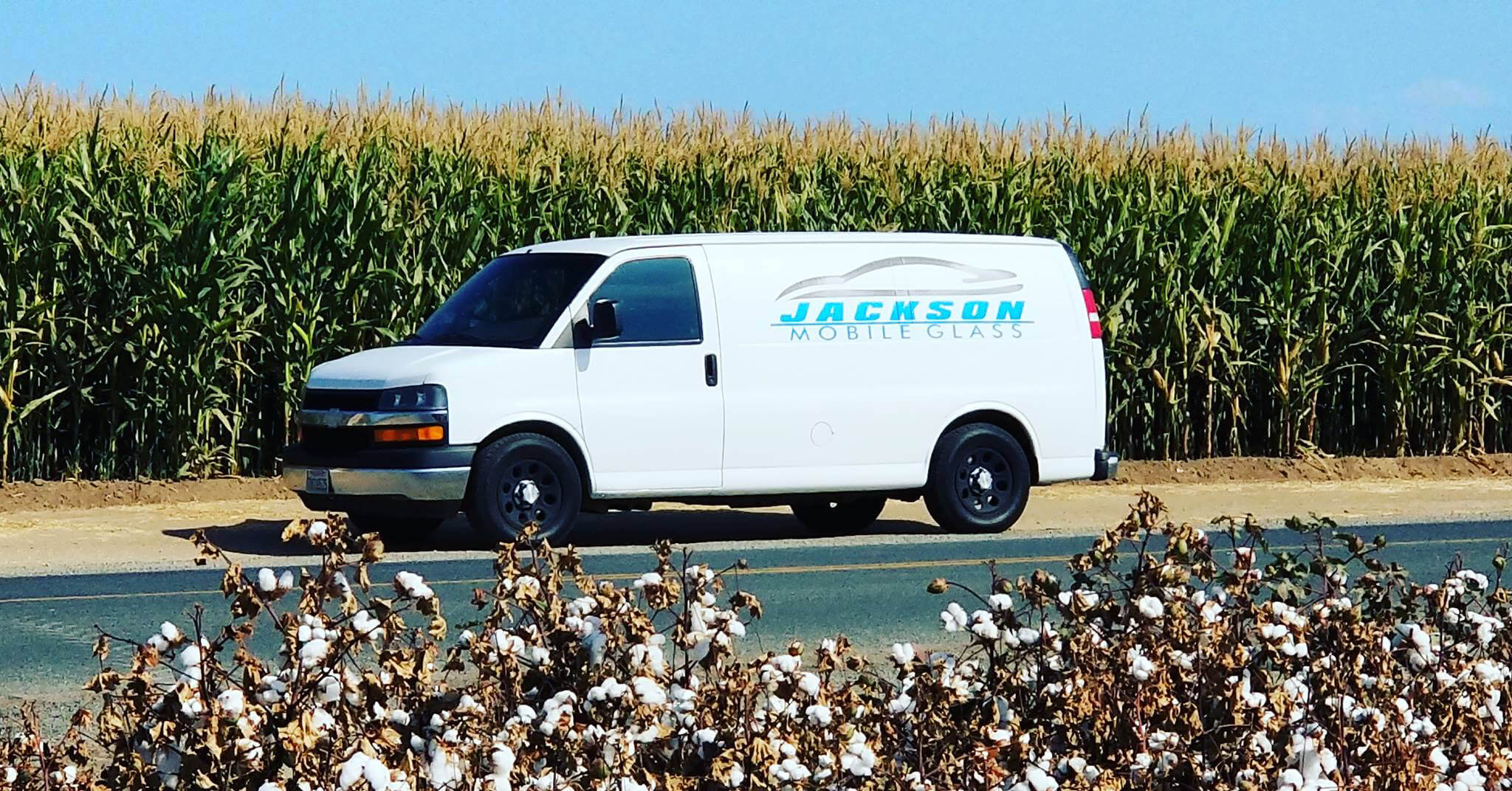 Auto glass repair. Jackson Mobile Glass utility van parked on the road between corn and cotton fields in Visalia, CA.